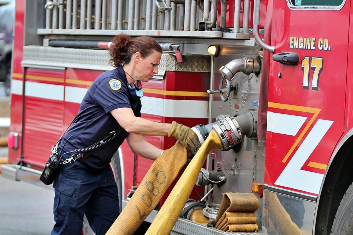 A woman firefighter connecting hose to a St. Paul fire engine